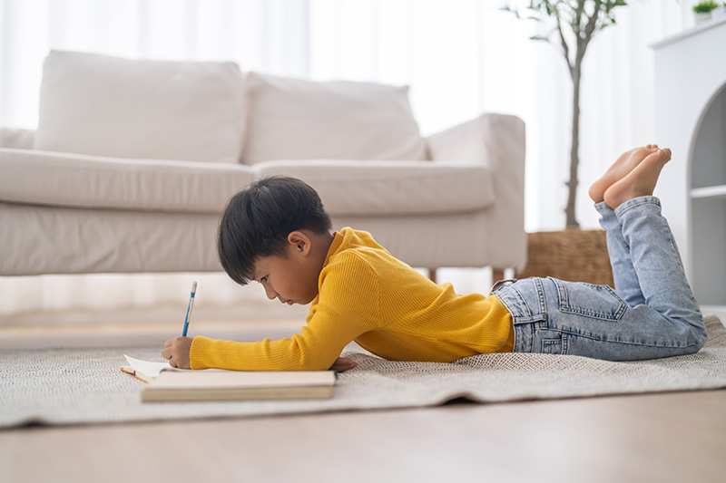 Asian American boy lying on the floor and writing