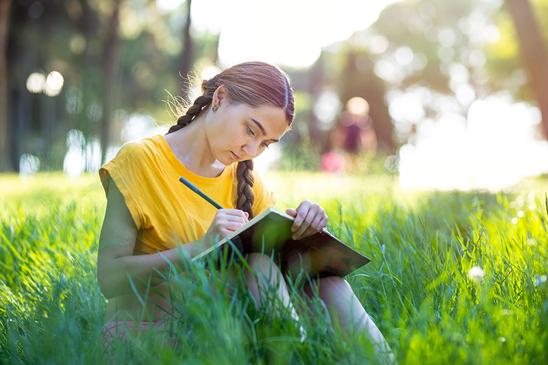 young girl writing in a notebook in tall grass
